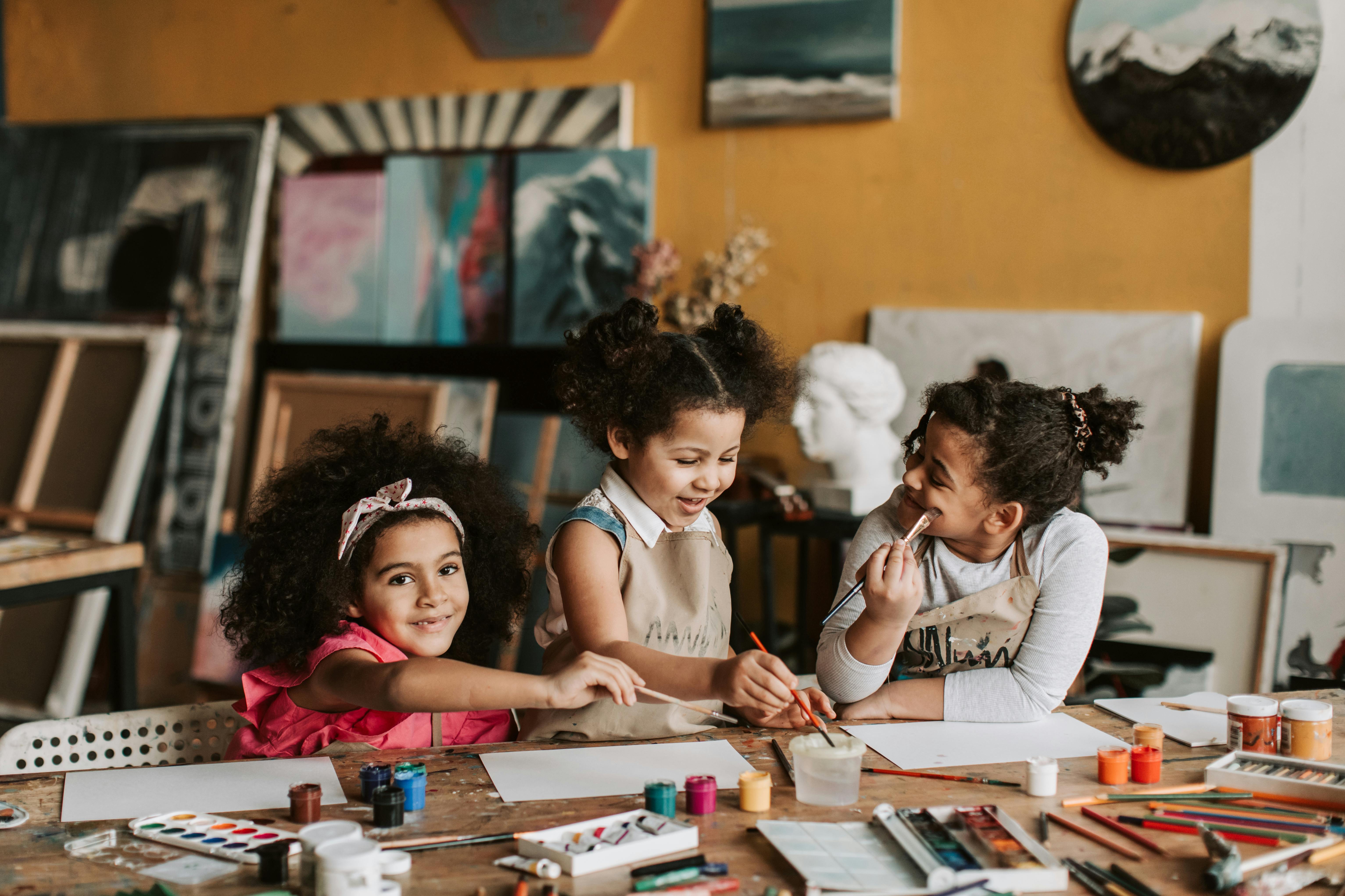 Three young girls painting together at a table.